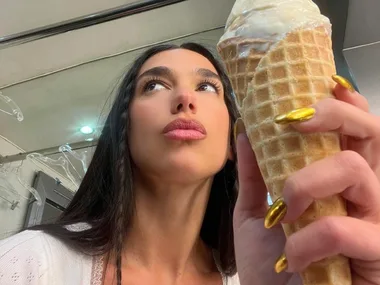 Woman with long hair holds an ice cream cone, showcasing metallic gold nails against a mirrored background.