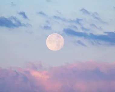 Full pink moon in a pastel sky with blue and pink clouds.