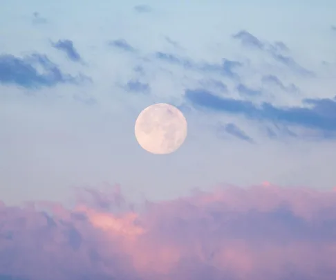 Full pink moon in a pastel sky with blue and pink clouds.