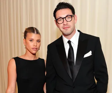 A couple dressed elegantly, with the woman in a black dress and the man in a black suit and tie, standing together.