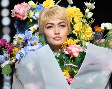 Model with short blonde hair wears a dress made of colorful flowers on a fashion runway.