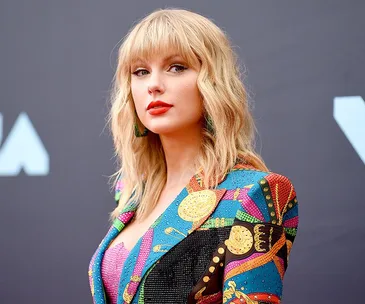 A person in a colorful patterned blazer poses confidently against a plain background.