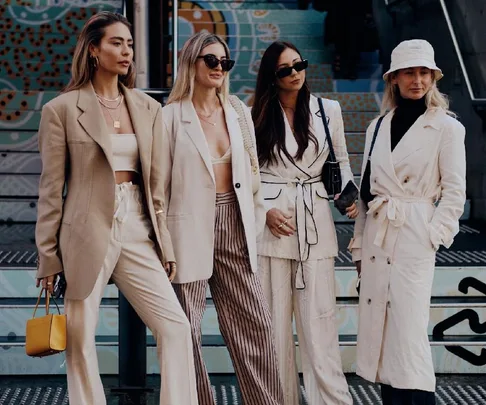 Four women in stylish neutral-toned outfits pose together outdoors at Australian Fashion Week.