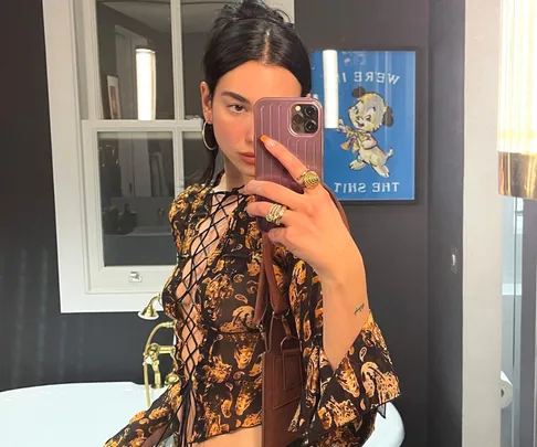 Woman taking a mirror selfie in a patterned top with a phone, standing in a stylish bathroom.