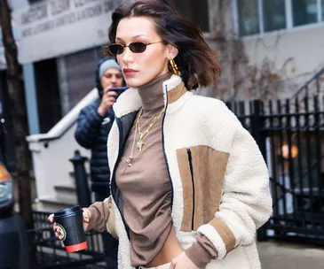 A woman in a stylish outfit holds a coffee cup, walking on a city street.