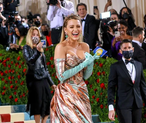 Blake Lively in a copper gown with mint gloves at Met Gala 2022, surrounded by photographers and attendees.