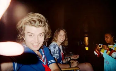 Three people on a film set, one in a sailor costume smiling at the camera, possibly related to "Stranger Things."