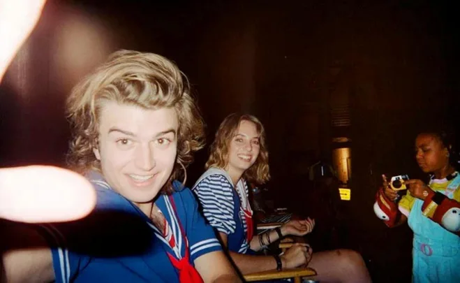 Three people on a film set, one in a sailor costume smiling at the camera, possibly related to "Stranger Things."