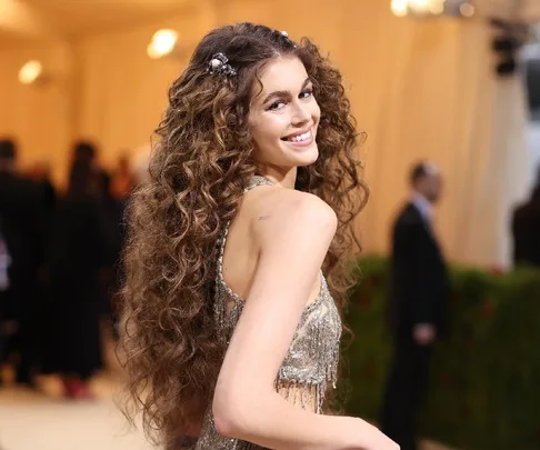 Young woman with long curly hair wearing a shimmering dress, smiling at the 2022 Met Gala.