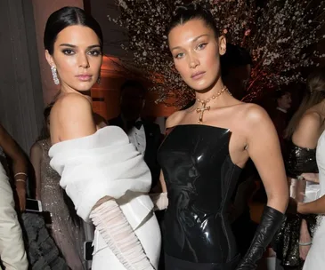 Two women in elegant gowns at a Met Gala after-party, posing in front of decorative branches.