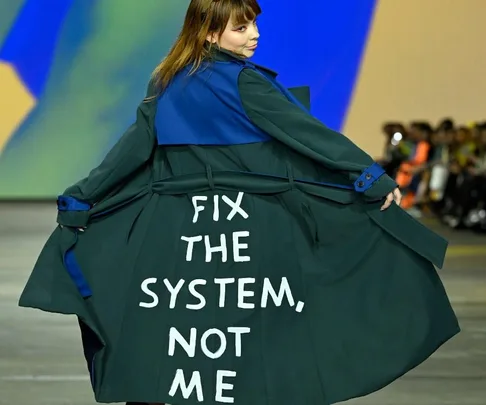 Model wearing a coat with "Fix the system, not me" message on runway at Australian Fashion Week 2022.