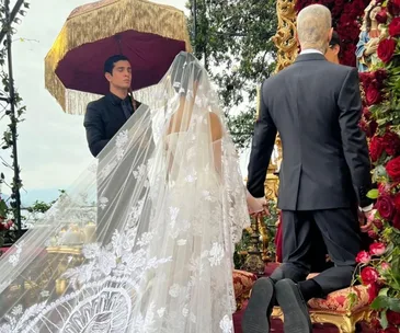 Wedding ceremony with a couple holding hands at an ornate altar with floral decor and a person under a decorative umbrella.