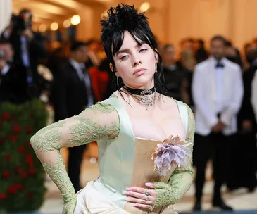 A person in a light green and cream gown with floral detail poses at a formal event, surrounded by people in formal wear.