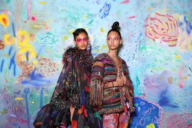 Two models in vibrant, colorful outfits against a painted abstract background at Afterpay Australian Fashion Week.