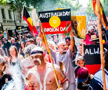 Crowd at a protest with signs like "Australia Day = Invasion Day" and "Sovereignty Never Ceded," highlighting Indigenous rights.