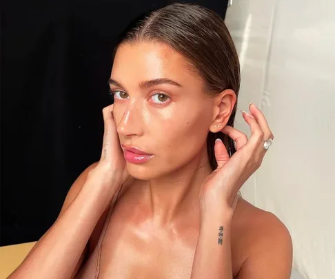 A woman with slicked-back hair poses with her hands near her face, highlighting her skincare routine.