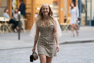 Camille walks down a Paris street in a plaid dress, smiling, from "Emily in Paris" Season 3.