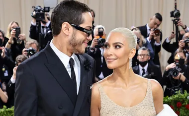 Couple smiling at each other on a red carpet, surrounded by photographers.