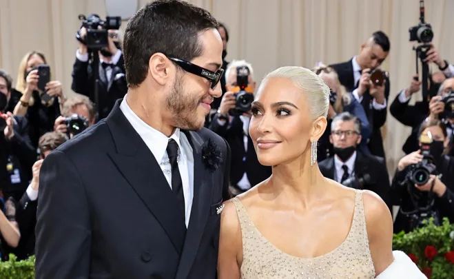 Couple smiling at each other on a red carpet, surrounded by photographers.