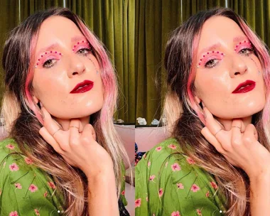 Woman with pink eye makeup and shiny red lips, wearing a green floral blouse, posing for the camera.