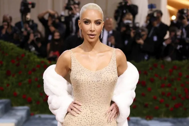 Kim Kardashian in a sparkling dress with a white fur stole at a high-profile event, surrounded by photographers.