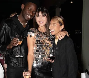 Three people at a party, smiling and holding drinks, with one wearing a shiny sequined top.