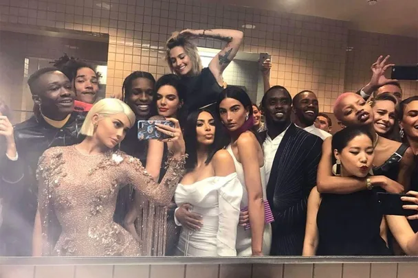 Group photo of celebrities in stylish outfits taking a selfie in a bathroom at the Met Gala.