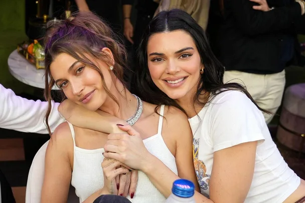 Two women sit closely together, smiling, one with her arm around the other in a casual setting.