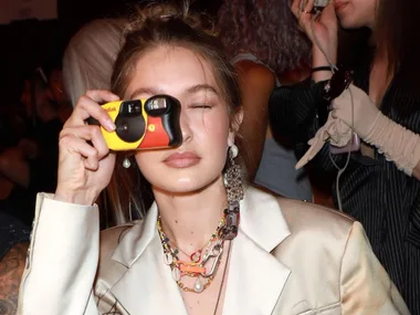 Person with long hair holding a yellow and black Kodak disposable camera to their face at an event.