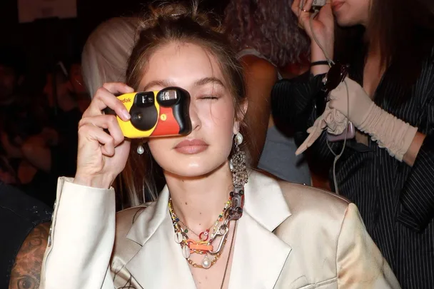 Person with long hair holding a yellow and black Kodak disposable camera to their face at an event.