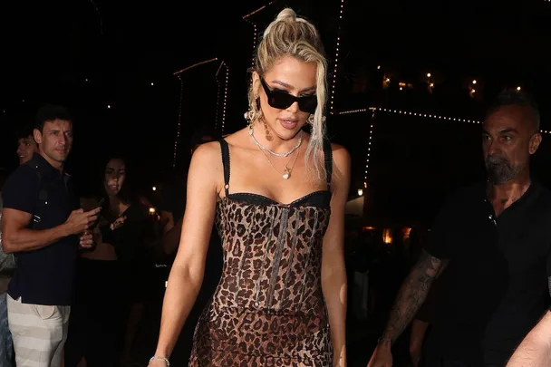 Woman in leopard print dress and sunglasses at a nighttime event, accompanied by people.