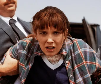 A girl in a plaid shirt looking distressed, being held by a man in a suit, near a vehicle.