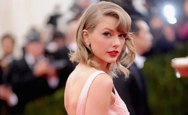 A woman with blonde hair and red lipstick in a pink dress at a formal event, surrounded by photographers.