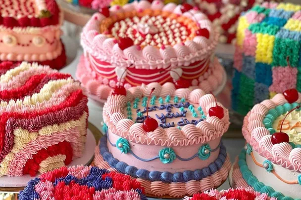 A collection of colorful, decorative birthday cakes with piped frosting, cherries, and vibrant patterns.