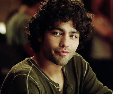 A man with curly hair wearing a green shirt looks to the side, captured in a candid moment.