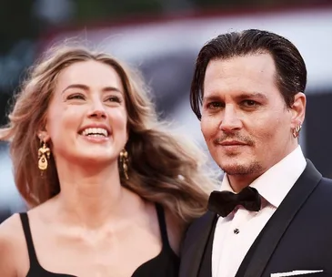 A woman laughing and a man in a suit are posing together on a red carpet event.