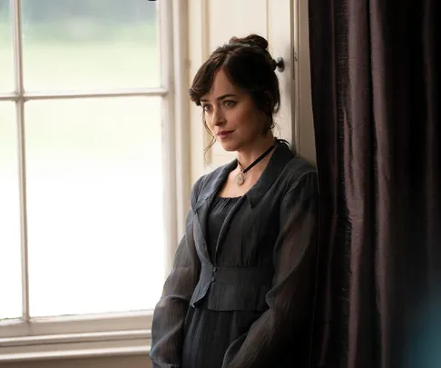 Dakota Johnson as Anne Elliot in period attire, gazing softly near a window, from "Persuasion" film adaptation.
