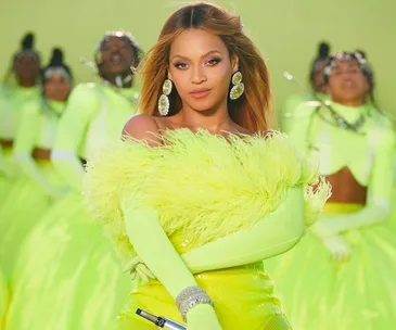 Beyoncé wearing a vibrant yellow feathered outfit with dancers in matching attire performing behind her.