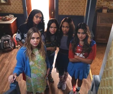 Five young women stand on a staircase, looking up with concerned expressions in a dimly lit room.