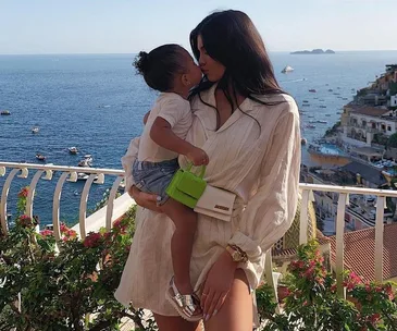 Woman holding a child, facing each other affectionately on a Mediterranean balcony with sea view.