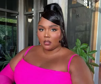 Woman in a bright pink outfit posing indoors with plants in the background.