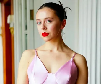 Person with red lipstick in a pink dress, standing in a well-lit room.