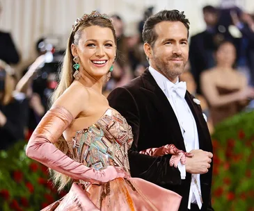 A couple dressed in elegant attire at a formal event, standing together smiling, with a blurred audience in the background.