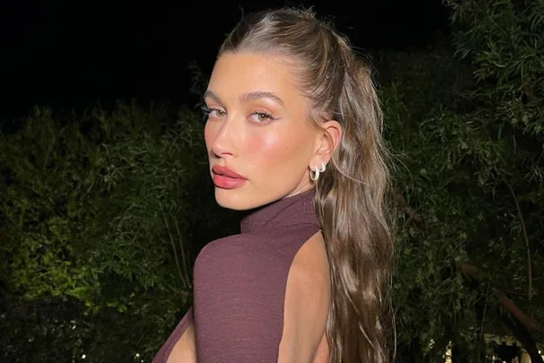 A person with long hair and hoop earrings in a dark top poses outdoors at night.