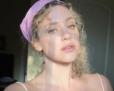 Woman with curly hair and pink headband in natural light. Article: "4 Things Making You More Pimple Prone".