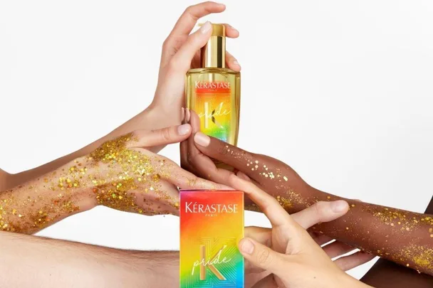 Hands holding a Kérastase hair oil bottle and box with a rainbow design, adorned with gold glitter.