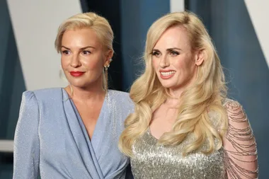 Two women with blonde hair in elegant dresses at an event, smiling at the camera.