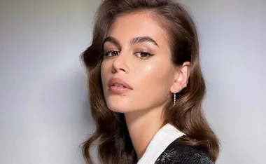 Young woman with wavy brown hair and subtle makeup, looks over her shoulder in a close-up shot.