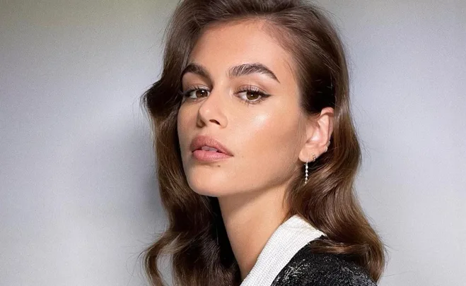 Young woman with wavy brown hair and subtle makeup, looks over her shoulder in a close-up shot.