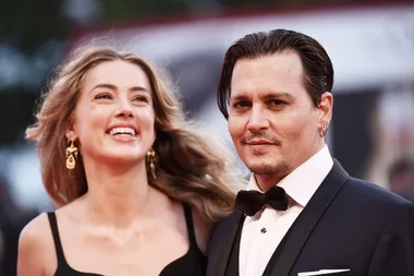 A man in a tuxedo and a woman in a black dress with earrings smiling at an event.